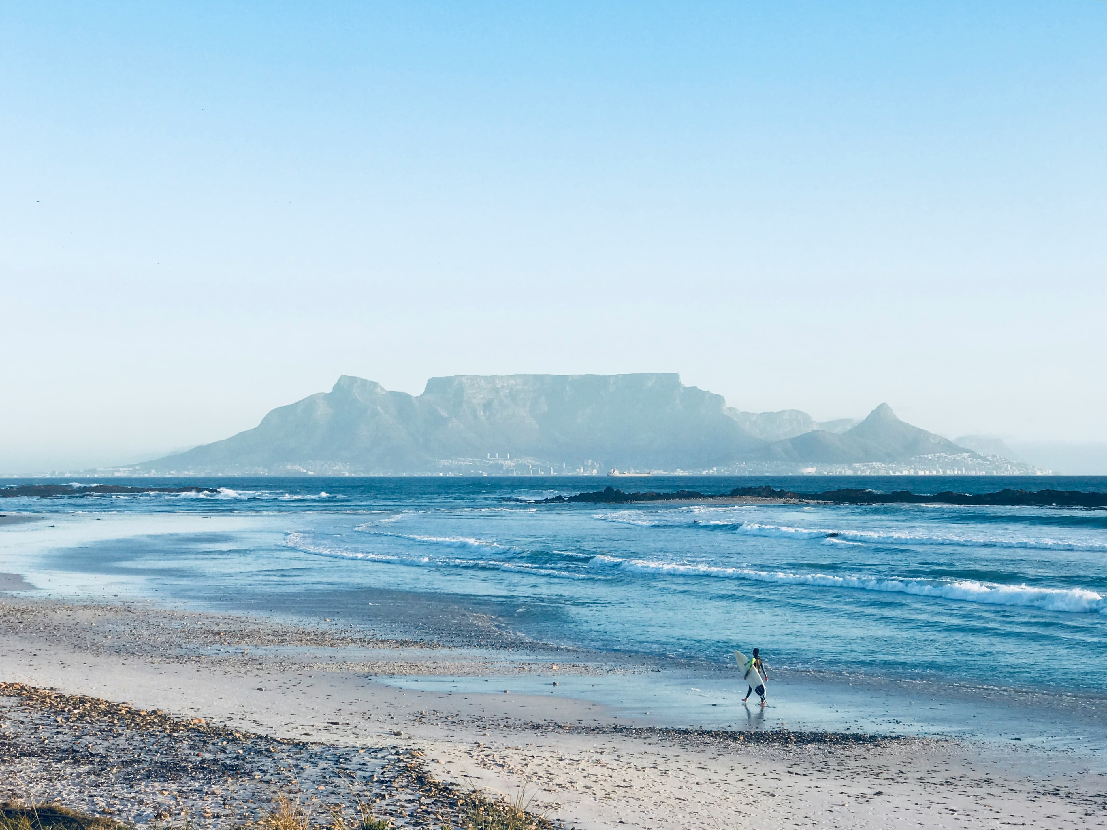 Surfer walking along Bloubergstrand Beach with Table Mountain in the background